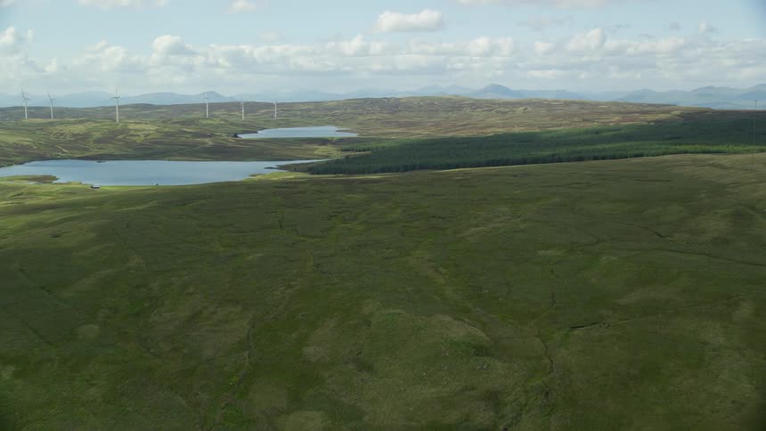 Aerial of grass covered hillsides with small lakes on the plateau with windmills on the land