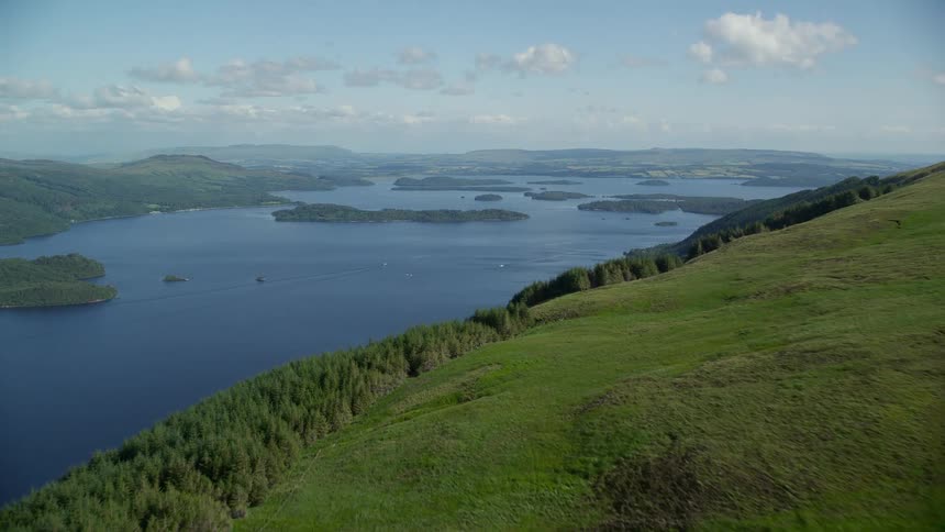 Aerial of a grass covered mountainside revealing a large river flowing through the landscape