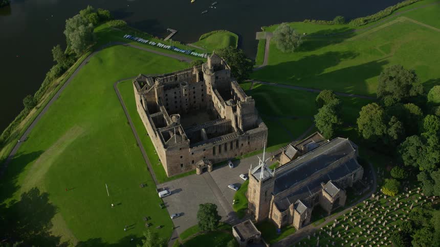 Aerial shot of a castle surrounded by grasslands next to a cliff on the coast during day time