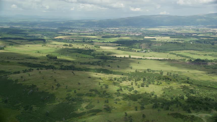 Aerial of a flat grassland in a rural area with buildings on the landscape and mountains on the horizon