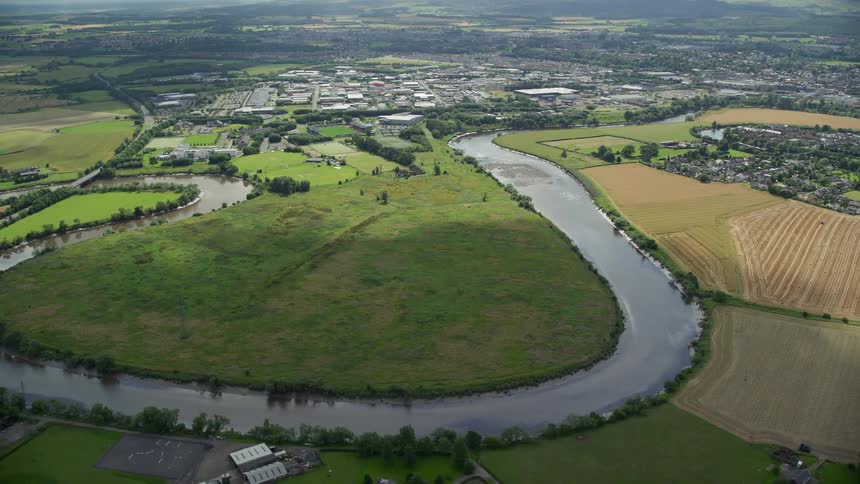 An aerial view of a river in a field that has vegetation and a small town in the background