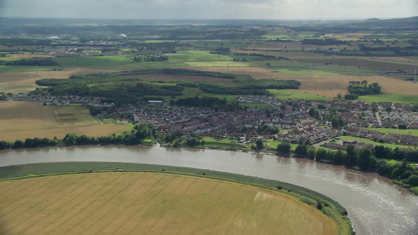 Aerial of a river winding around fields near a village with houses in a rural area