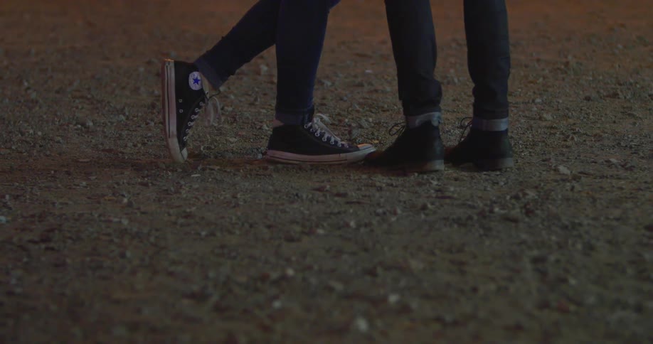 Two people wearing sneakers and jeans standing in dirt as seen from the waist