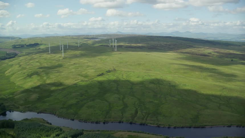 A huge field of grass and a river and right in the background is a windmill farm