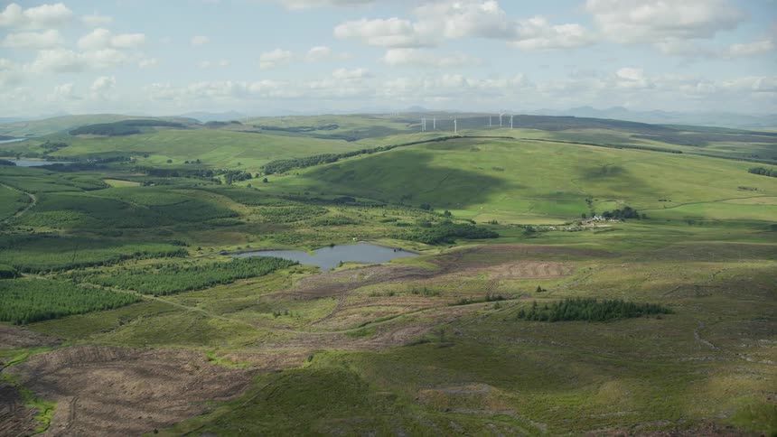 Aerial of a rural forest and field with a small pond in the field valley near a hillside
