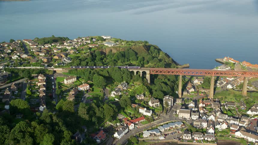 Aerial view of an urban area by the sea with a lot of train tracks where a train is passing