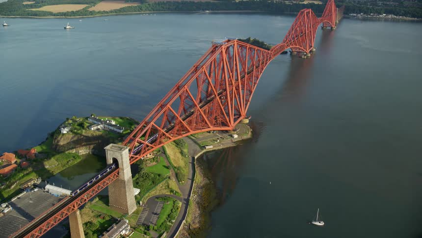 Aerial of a bridge going over a river with a train traveling over it on a bright sunny day