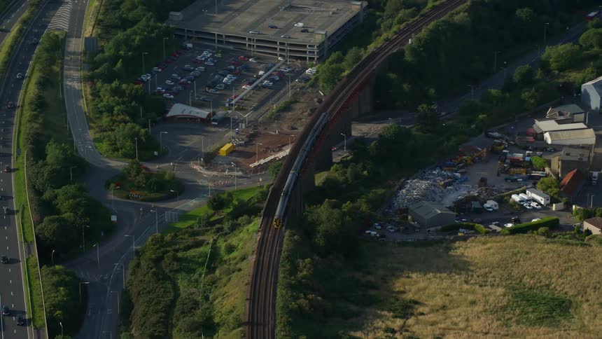 Aerial view of a train passing over a bridge in an urban area with a highway beside it