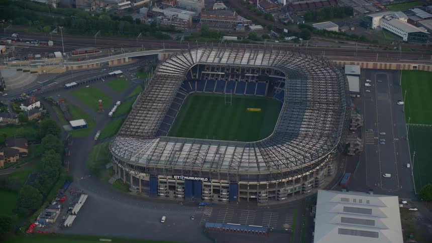 A large stadium with a lawn in the middle and a parking lot on the side