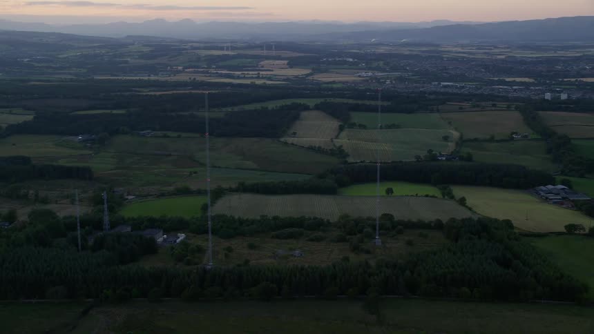 Two very tall antenna towers are located in a rural area with many fields