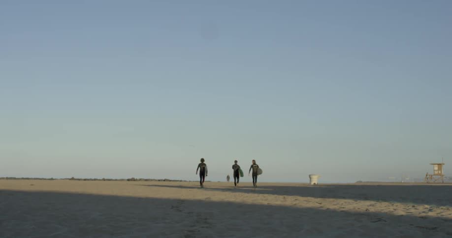 Three surfers walk along a beach