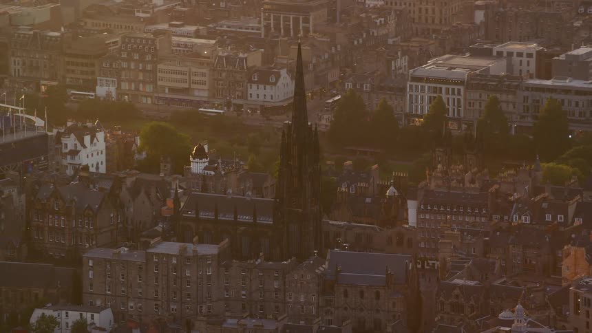 Drone view of city buildings with a tall steeple as the sun shines through over the buildings