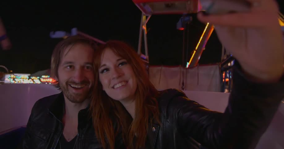A woman takes a selfie on a carnival ride with a man