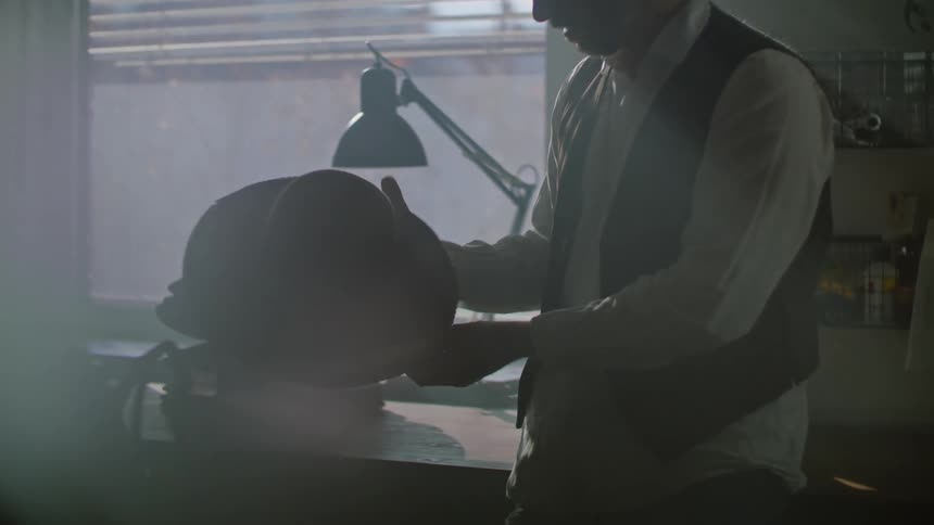 A man in his workshop uses a tool to make a hat with a brim