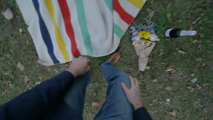 A person puts a blanket on the grass to rest with a flower bouquet