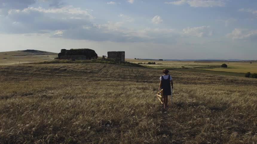 Artist carries easel across field toward buildings on hill
