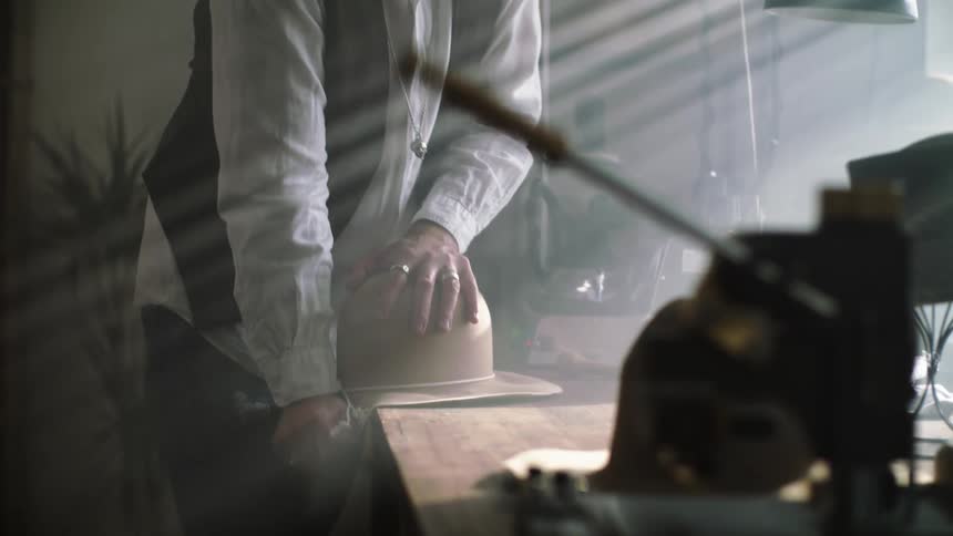 Hatter shapes hat while working in workshop