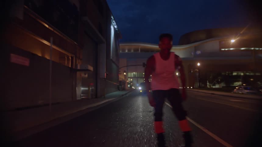 Skater skates on street followed by car at night