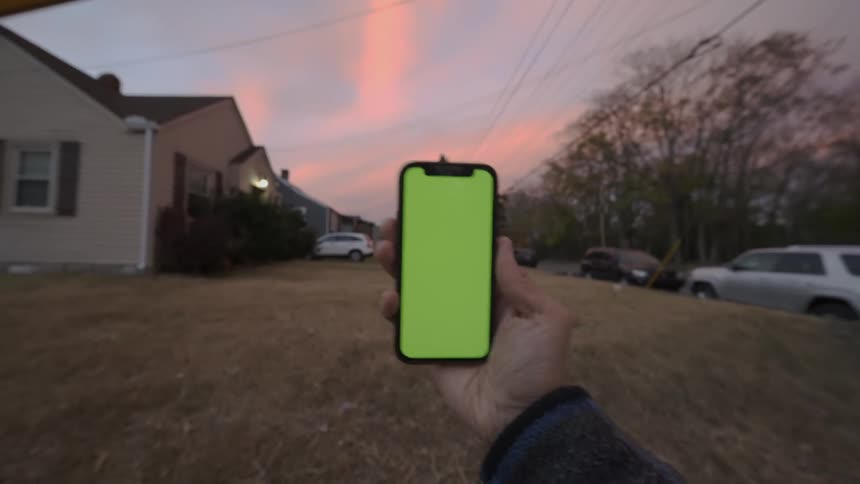 Person walking along residential street with smartphone turns toward person walking in their driveway at sunset