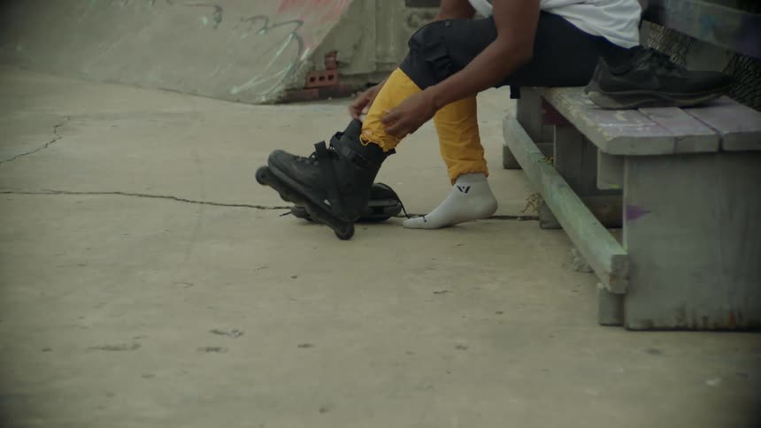 Man sitting on bench in park across from apartment building puts on inline skates
