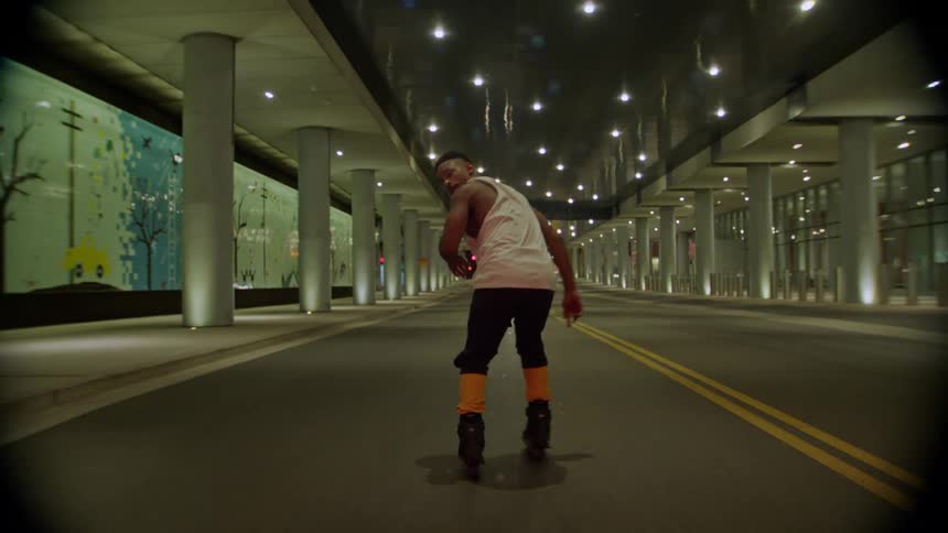 A young boy rollerblades through the city at night