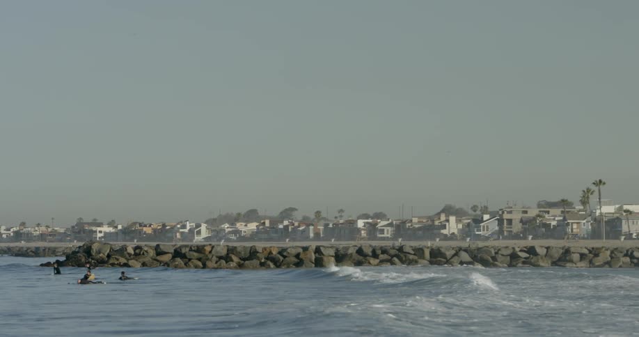 Waves crash against the shore as people surf nearby