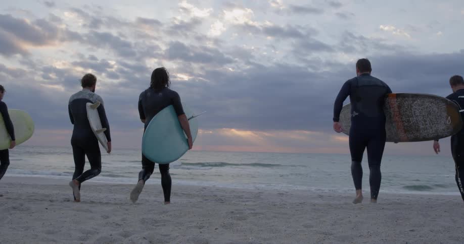 Five surfers carrying their boards towards the water on a beach