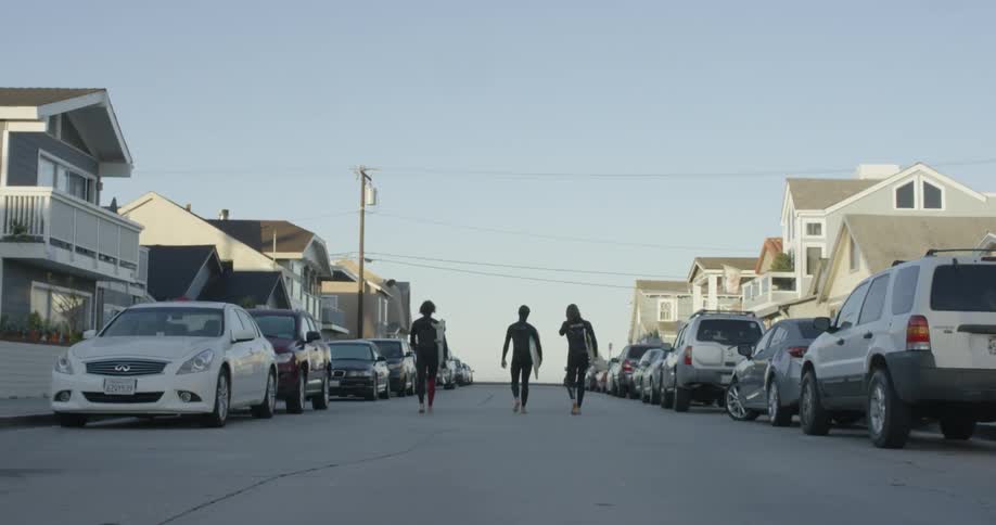 Three men carrying their surfboards down a street
