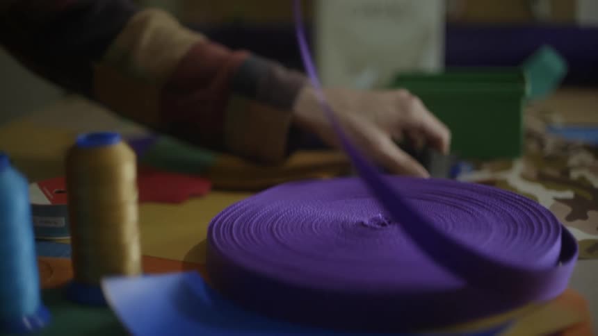 A persons hands grabbing purple ribbon and sliding it through a clasp on their craft table