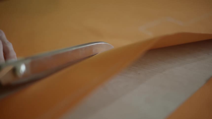 A person uses a large pair of scissors to cut a long piece of fabric