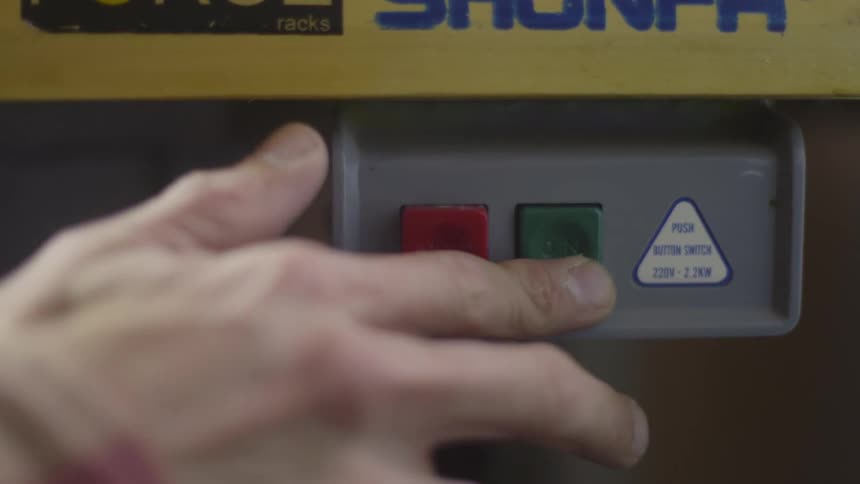 A person reaches out and presses a green button on a machine