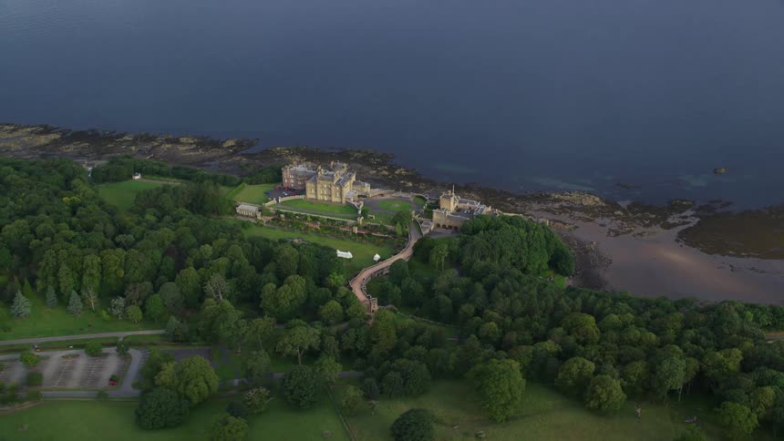 Aerial view of a mansion by the sea in a natural setting with conifers and fields