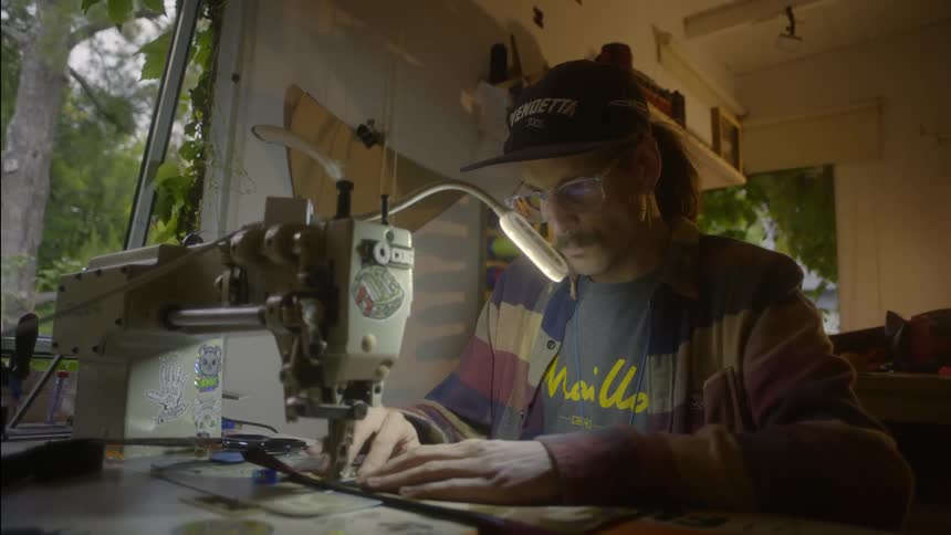 Male tailor with cap ponytail mustache and glasses uses sewing machine
