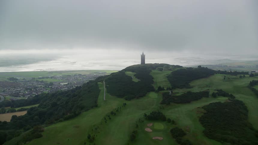 Drone view of a grassy hillside with a tower on the top in a rural neighborhood
