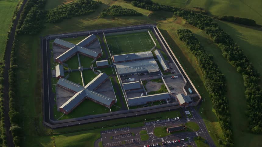 Aerial of buildings in a fenced area bordered by trees at midday