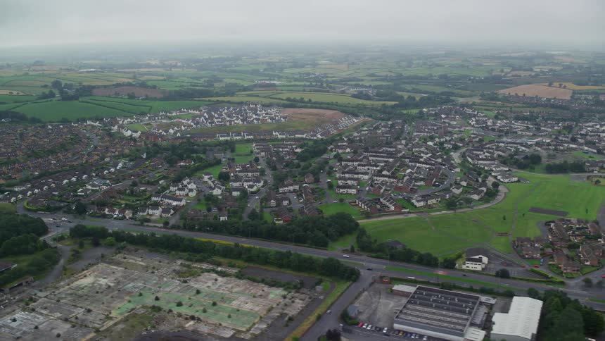 Aerial of buildings roads cars trees in a suburban area at midday