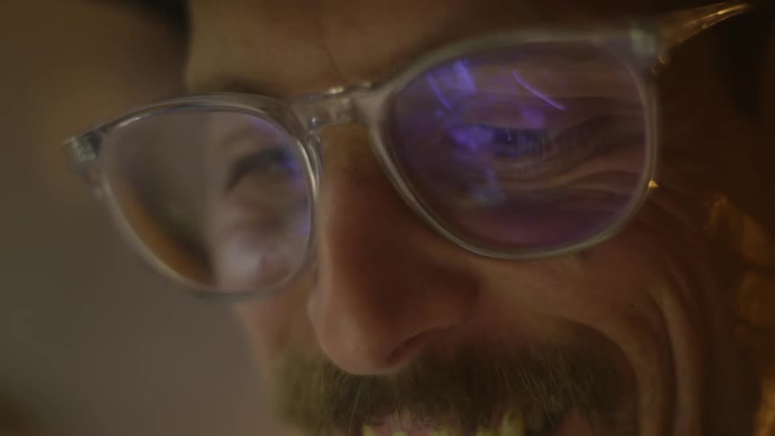 A man wearing glasses looks down at a screen while smiling