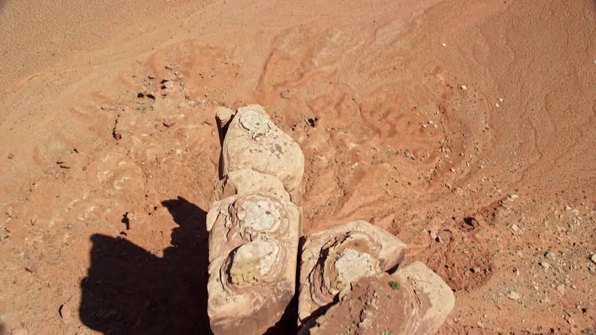 Narrow rock formation casts shadow onto arid red ground