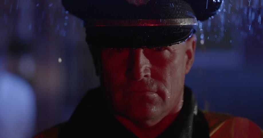 A police officer stands outside at night in the rain