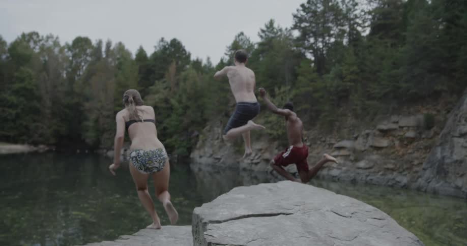 Three people jump off a small cliff into a lake