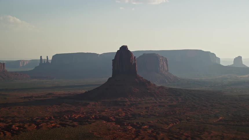 Aerial of a butte formation in the desert with a mesa mountain in the background