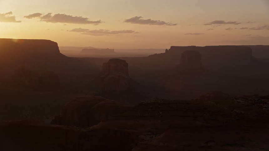 Drone view of the sun shining over rocky mountain formations in the desert casting shadows in the canyons