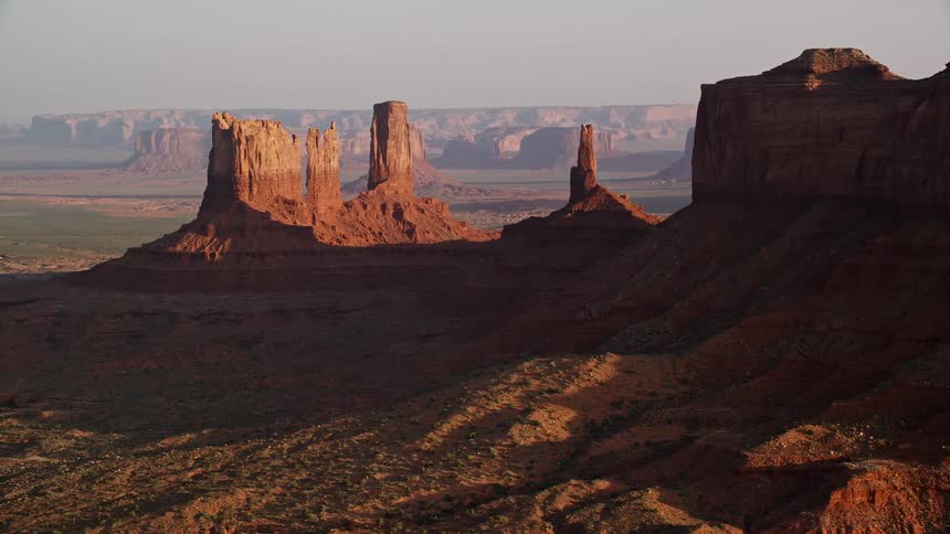 Aerial of butte formations in the desert on a sunny day with mesa formations in the distance