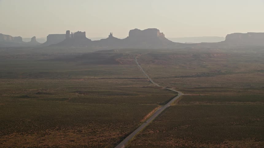 Drone view of a roadway going through a flat grass land in the desert toward rock formations on the horizon