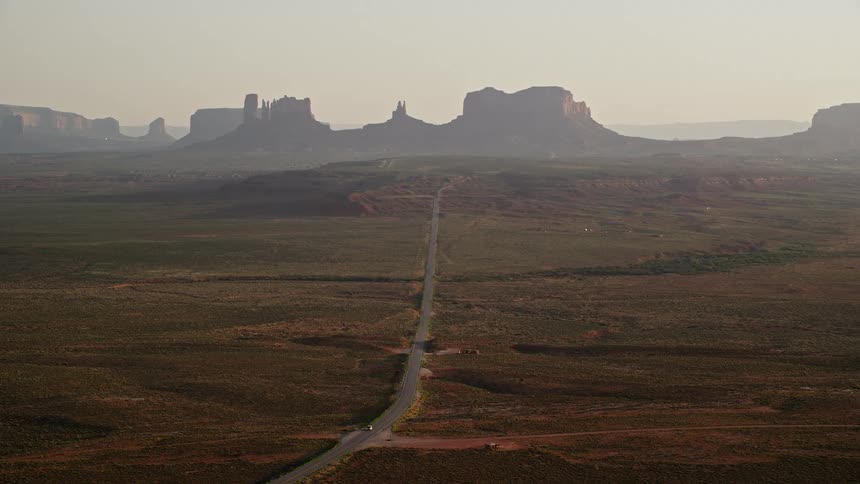 Aerial of a road going through the desert flat land with mountains on the horizon