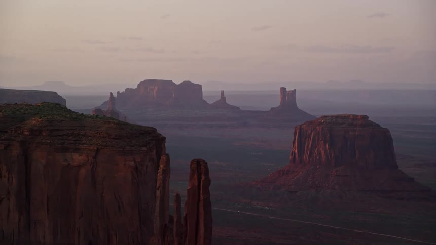 Aerial of butte formations and large mesas with plateaus on the top in the desert with a single road traveling through