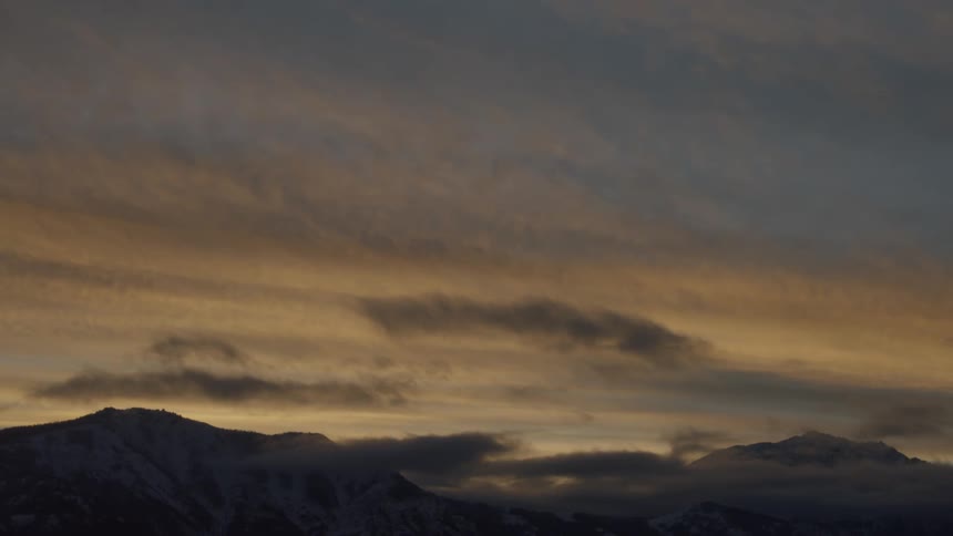 Mountains on a horizon with the sun casting rays across the wispy cloudy sky
