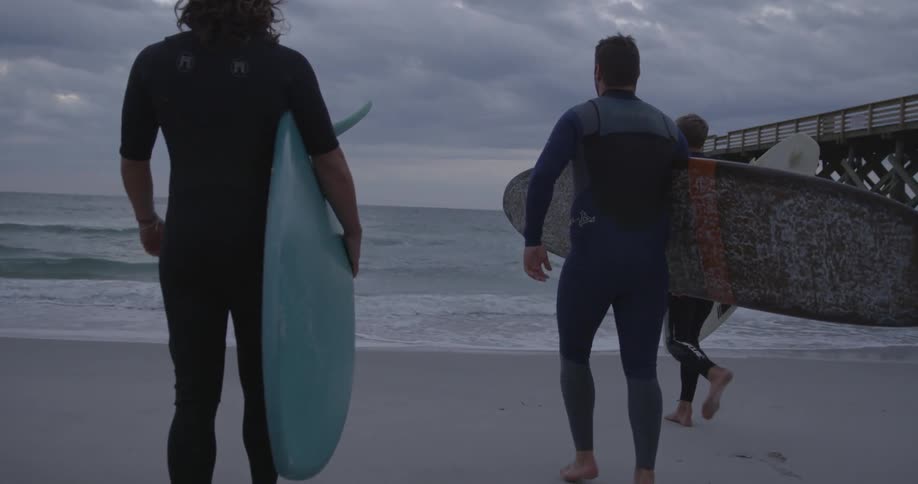 People walk towards the water with surf boards