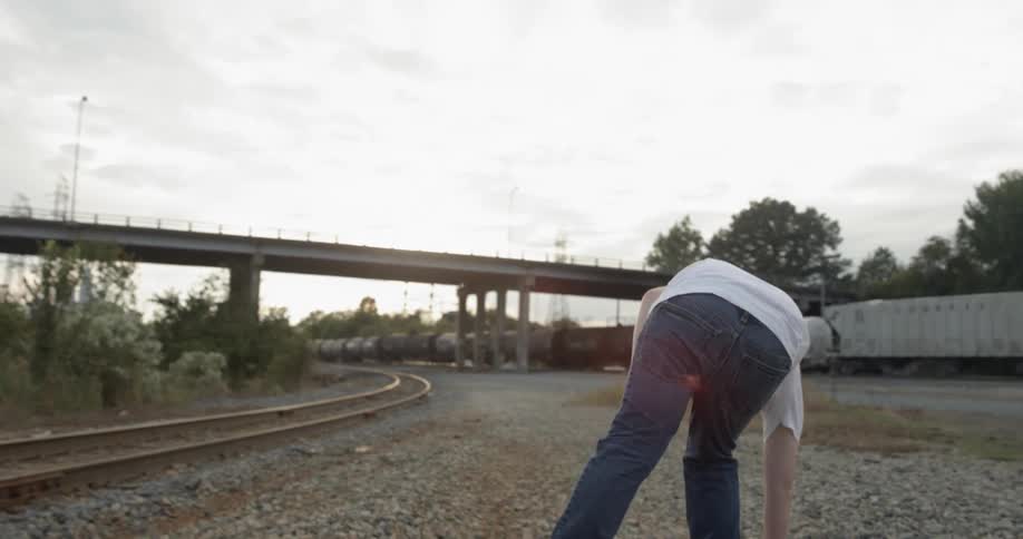 Young boy walking along railroad tracks and throwing a stone