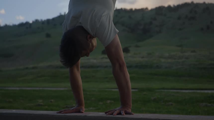 Man performs a handstand across road from hill on a cloudy day